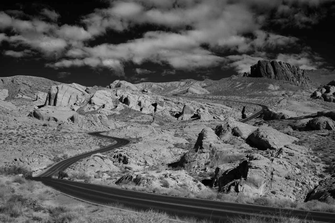 Paysage en noir et blanc de la route qui serpente dans Valley of Fire dans le Nevada. Photographie par Amar Guillen, artiste photographe